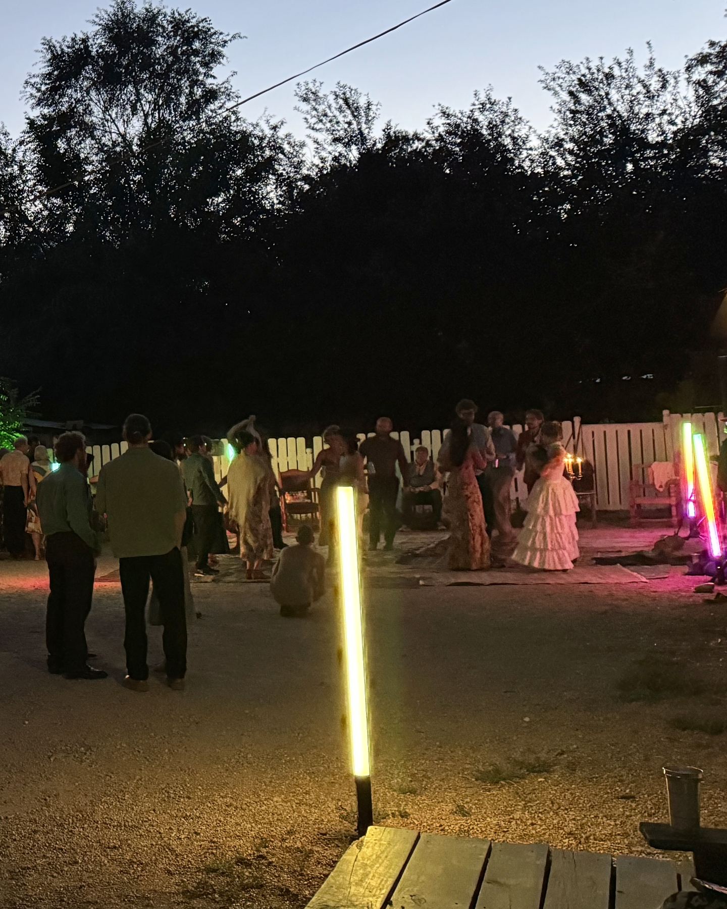 Wedding guests dancing at dusk in the barn yard, lit by tube lights